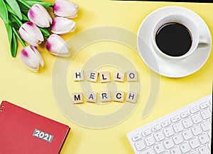 Flat lay of woodeng letters HELLO MARCH , coffee cup ,tulip flower bouquet, red diary2021  and computer keyboard on yellow