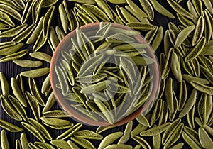 Top view of foglie spinach pasta in bowl and scattered on black wooden table