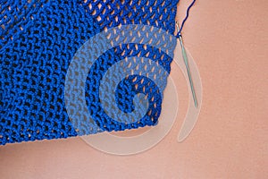 Top view of folded blue crochet net with a hook inside of the loop, top view, beige paper background.