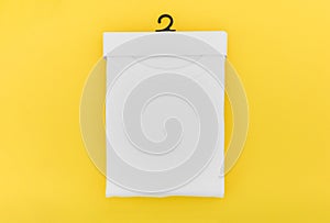 Top view of folded white color t-shirt in paper hanging package on yellow background, copy space, flat lay