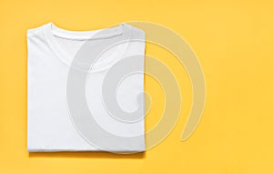 Top view of folded white color t-shirt on yellow background, copy space, flat lay