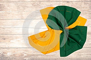 Top view of a folded yellow and green kitchen cloth, textile, tablecloth or napkin on blurred wooden background. Template for your