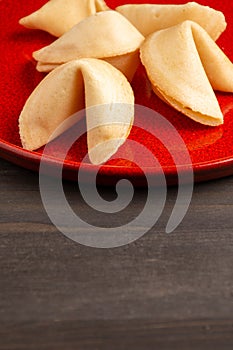 Top view of fortune cookies on red plate, on dark wooden table, in vertical