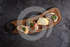 Top view on Four bruschettas lay on wooden board. Appetizers with tomato, mozzarella, pesto, salmon and roast beef on a gray