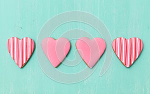 Top view on four pink sugar cookies in heart shape on turquoise wooden background. Valentine`s day card