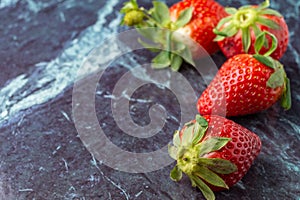 Top view of four strawberries on blue marble, with selective focus, horizontally