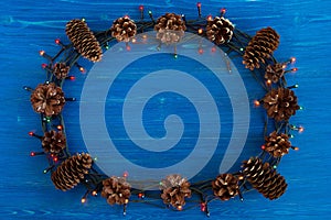 Top view on frame from Christmas lights and pine cones on the blue wooden background.