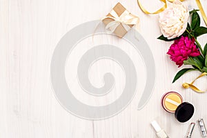 Top view frame made of women items : cosmetic, peony flowers, lipstick, gift box on wooden background. Minimal flat lay style