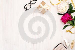 Top view frame made of women items : cosmetic, pion flowers, purse, gift box on wooden background. Minimal flat lay style