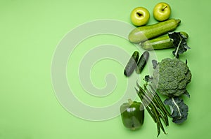 Top view of fresh asparagus, broccoli, pepper, cucumber, apples, marrows on the green background.Empty space