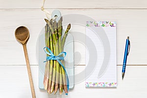 Top view of fresh asparagus on a wooden table with recipe notebook and ballpoint