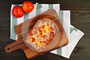 Top view of fresh baked homemade pizza toast on breadboard with fresh tomatoes on kitchen cloth