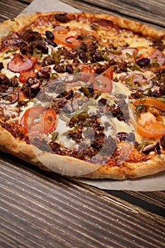 Top view of fresh baked pizza with meat and vegetables on a wooden table. Pizza delivery. Take away.
