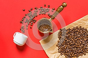 Top view of fresh coffe prepared in  cezve traditional turkish coffee pot, whte cup and coffee beans on craft paper on red