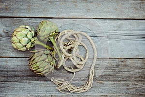 Top view Fresh green artichokes with braided rope on vintage wooden kitchen table. Farmer local market. Selective focus, Copy