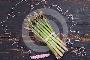 Top view on the fresh green asparagus bunch decorated with pink thread on the black wooden background. Healthy spring vegetables