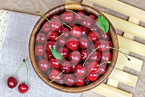 Top view of fresh juicy red sweet cherry berries in the wooden bowl on light background in summer.