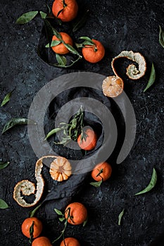 Top view of fresh mandarin oranges or tangerines with leaves on textured dark background.