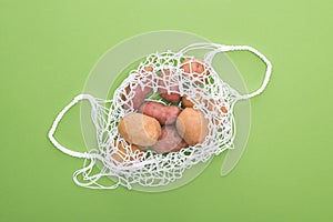 Top view of fresh potatoes in eco friendly string bag isolated on green.