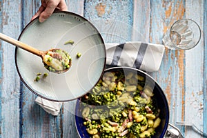 Top view on fresh prepared broccoli with gnocchi in casserole dish on the wooden table - hand of unknown person putting homemade