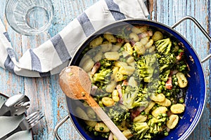 Top view on fresh prepared broccoli with gnocchi in casserole dish on the wooden table - homemade healthy food in bright light