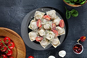 Top view on fresh ravioli with slice cherry tomato on black plate and dark background.