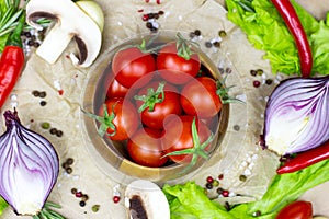 Top view of fresh red ripe cherry tomatoes in wooden bowl with salad leaves, onion, pepper, champignon mushrooms, spices and salt