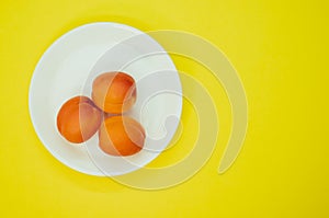 Top view of fresh three apricots on a plate isolated on yellow background