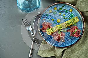 Top view on fresh tuna tartare with bread, onion in blue plate on wooden background. Restaurant food. Flat lay with copy space