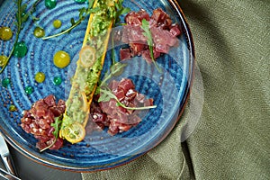 Top view on fresh tuna tartare with bread, onion in blue plate on wooden background. Restaurant food. Flat lay with copy space