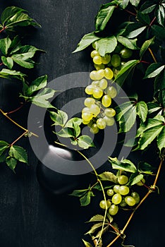 top view of fresh white grapes with green leaves and bottle of wine on dark wooden