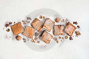 Top view of freshly baked home made brownie cake arranged with nuts, chocolate and cocoa powder over white rustic background