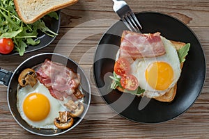 Top view of fried eggs on black plate and pan with fork, mushrooms and rukkola