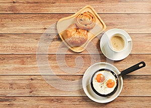 Top view of fried eggs in pan , cup of coffee and  danish pastry and Croissant on wooden background