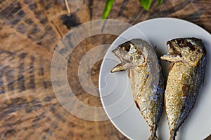 Top view fried mackerel on a white plate with real wooden table with copy space for text or design. Fried fish on the dish