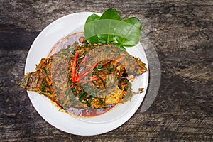 top view Fried Nile tilapia fish with red curry paste on white plate wooden background, Thai food is spicy mixed with sweet flavor