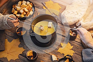 Top view friends cooking Swiss fondue assorted cheeses dinner on fire, hands holding mulled wine background wood board