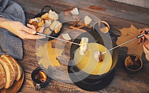 Top view friends cooking Swiss fondue assorted cheeses dinner on fire, hands holding mulled wine background wood board