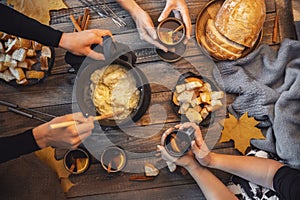 Top view friends cooking Swiss fondue assorted cheeses dinner on fire, hands holding mulled wine background wood board