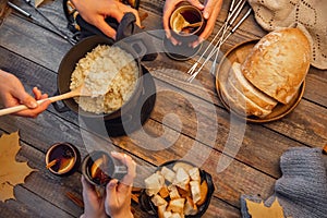 Top view friends cooking Swiss fondue assorted cheeses dinner on fire, hands holding mulled wine background wood board