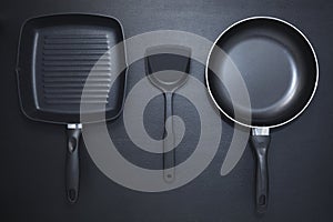 Top view frying pan and plastic spade on black table background.