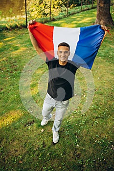 Top view full-length portrait of young smiling man holding flag of France isolated over natural background