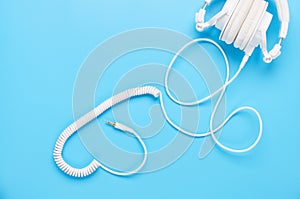 Top view upon gadgets on blue background, the composition of white headphones and wires in the shape of a heart