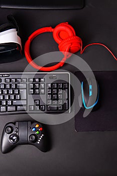 Top view a gaming gear, mouse, keyboard, joystick, headset, VR Headset on black table background.