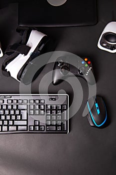 Top view a gaming gear, mouse, keyboard, joystick, headset, VR Headset on black table background.