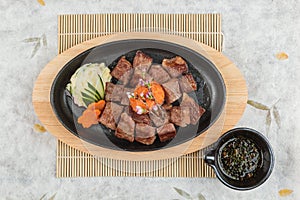 Top view of Garlic Saikoro Steak: medium rare dice wagyu topping with mince carrot on hot plate served with potato salad.