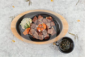 Top view of Garlic Saikoro Steak: medium rare dice wagyu topping with mince carrot on hot plate served with potato salad.