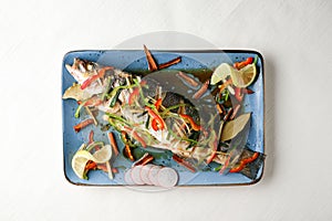 Top view of a garnished fish with vegetables on a blue plate