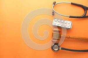 Top view of gavel, stethoscope and pills on orange background