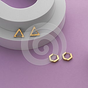 Top view of geometric earrings pairs on white arch on purple background with copy space